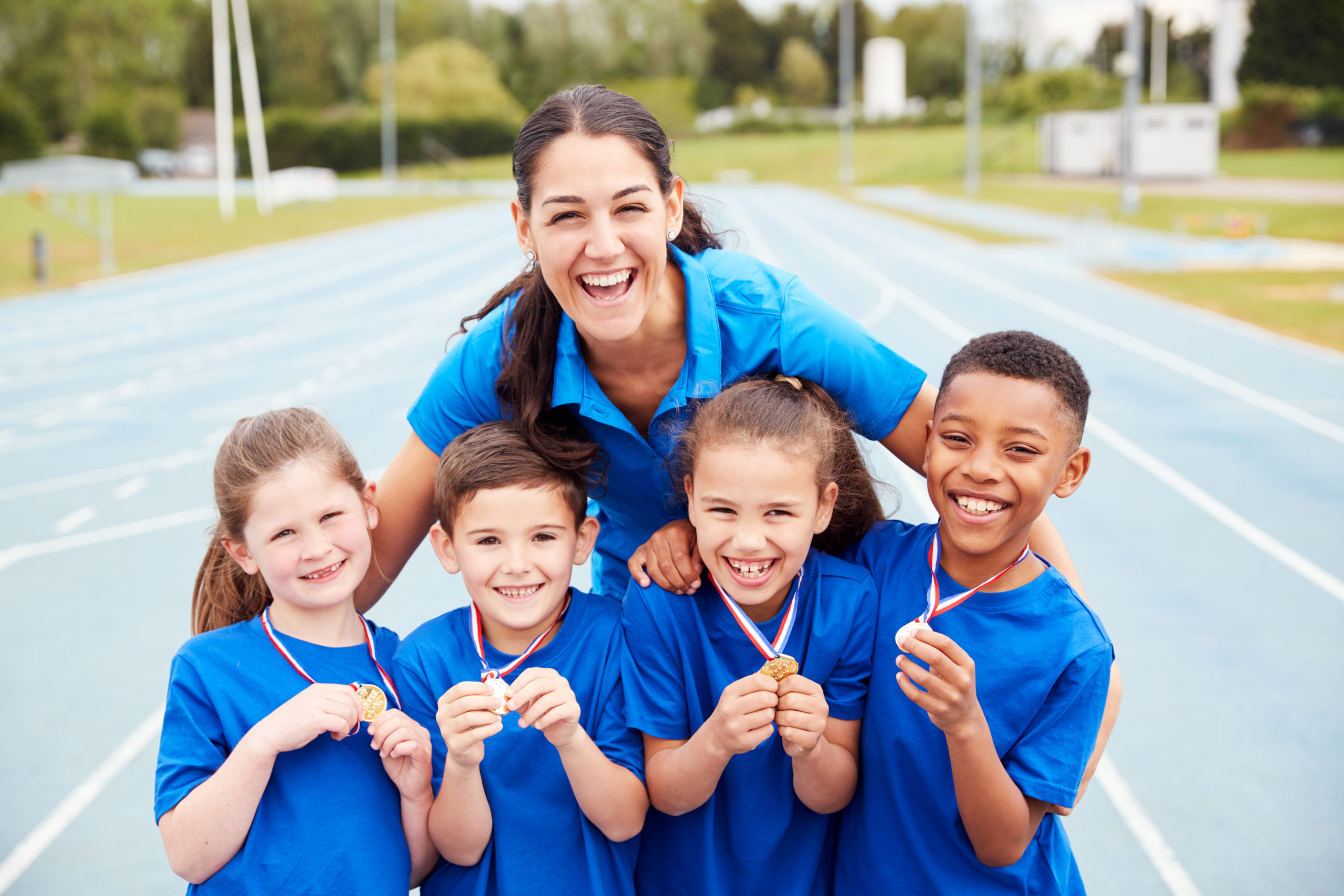 Portrait Of Children With Female Coach Showing Off Winners Medals On Sports Day